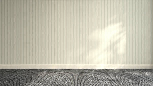 istock Front view of empty room with cream colored wallpaper wall with vertical stripe, baseboard and black carpet floor in dappled sunlight from window 1440660688