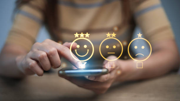 istock Customer service evaluation concept. smiling Asian female Is using a smartphone And she is pressing face emoticon smile in satisfaction on virtual touch screen. 1440671263