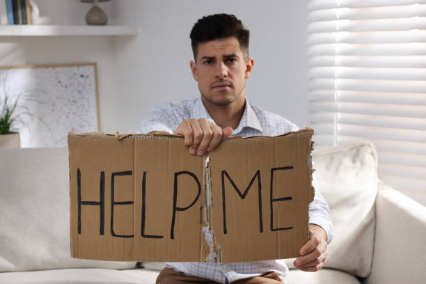istock Unhappy man with HELP ME sign on sofa indoors 1440679835