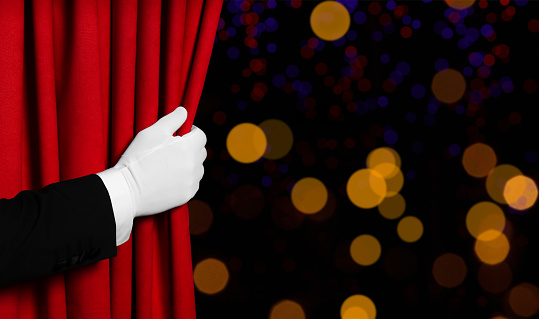 Man opening red front curtain against blurred lights. Bokeh effect