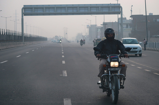 Delhi, India - November 7, 2022: Stock photo showing view from car windscreen of traffic;  motorcycles, cars and taxis seen travelling in a polluted foggy tailback on a multilane highway.