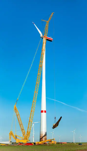 Construction work of wind turbine. crane is holding, grabing a blade of a wind turbine. Building and assembling a windturbine. Green energy, ecology and CO2-footprint reduction concept. Wörrstadt