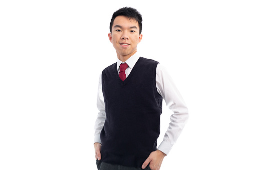 Medium shot of a young teen Asian boy in the studio with broad flash lighting. He is posing for a photo and grinning at the camera. He is wearing the school uniform of a white shirt with a white tie and a black sweater vest. The background is white.