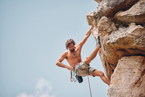 Mountain or rock climbing, cliff hanging and adrenaline junkie out on adventure and checking his safety equipment, hook and rope. Fearless man doing fitness, exercise and workout during extreme sport