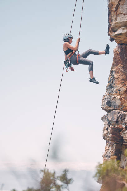 mujer escalando montaña con cuerda, actividad al aire libre en la naturaleza y ejercicio físico. escalada en roca de acantilados, aventura montañera y riesgo de peligro de acción. equipo de seguridad, tierra pacífica y motivación por la libertad - rápel fotografías e imágenes de stock