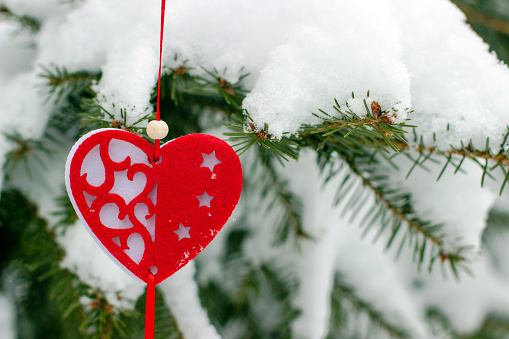 Heart-shaped Christmas tree decoration on spruce branch covered with snow