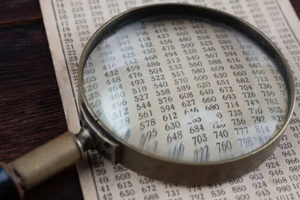 Photo of Retro cipher and cryptanalysis. Old vintage magnifying glass with calc table.