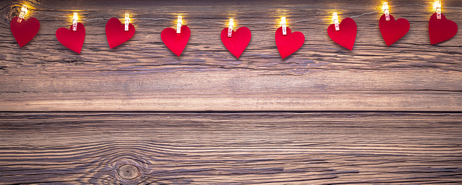 Valentines day copy space background with string lights and paper hearts on wooden texture.