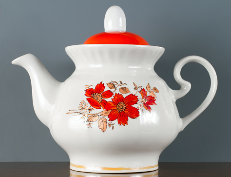 Porcelain teapot on a grey background. A teapot with a red floral pattern.