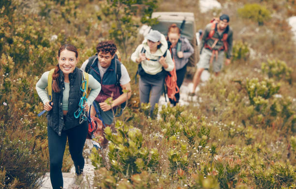 grupo de amigos camina por el sendero montaña arriba, para acampar en el paisaje natural en unas vacaciones de aventura extrema. un equipo de personas exploran la tierra juntos, en un viaje de senderismo a las montañas o colinas mientras están de vacaci - mochilero fotografías e imágenes de stock