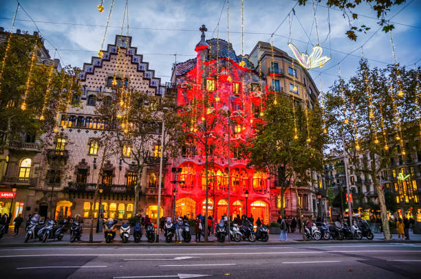 Barcelona, Spain - December 1, 2021: tourists in front of Casa Batllo designed by Antoni Gaudi and Casa Amatller in Passeig de Gracia in Barcelona at night lighted in red for the Christmas season.