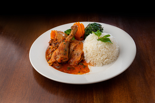 Chicken stew and rice dish served on a white place on a wooden table. Delicia African chicken stew with rice