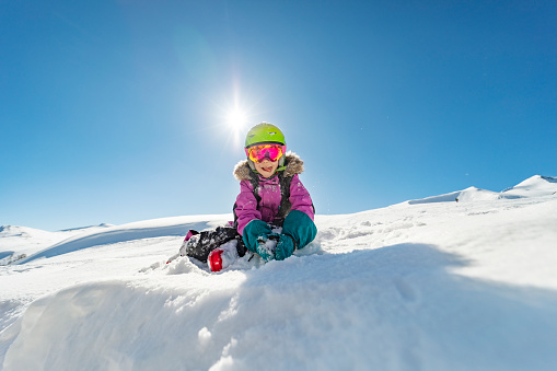 Little girl playing with snow in mountains while skiing