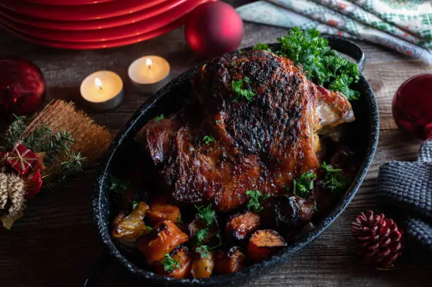 Roasted turkey shank for christmas dinner or lunch with vegetables. Served in a old fashioned roasting pan on wooden table with red plates, candle lights  and ornaments