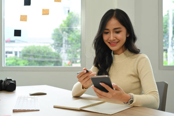 istock Attractive young female freelancer sitting front of computer pc and using mobile phone for checking social media. 1440700476