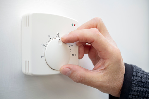 Man regulating heating temperature with a modern wireless thermostat installed on the wall at home.