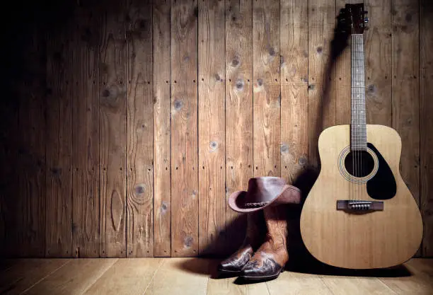 Photo of Acoustic guitar, cowboy hat and boots against blank wooden plank panel grunge background with copy space