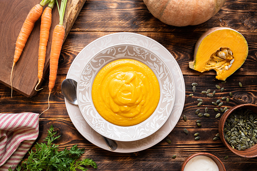 Pumpkin and carrot vegan soup on dark wooden background. Autum/fall recipes.