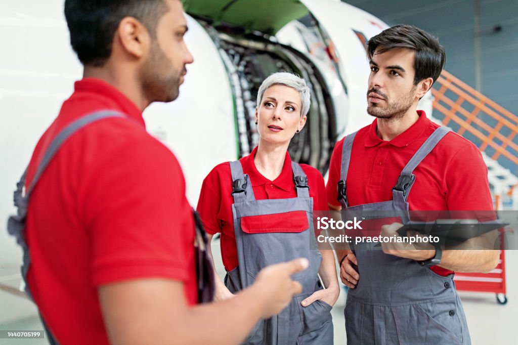 Airplane mechanics discussing planned aircraft maintenance in a hangar Adult Stock Photo