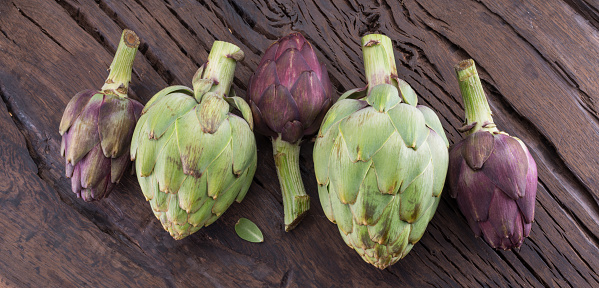 Green and purple artichoke flower edible buds on wooden background.