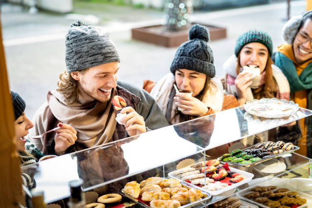 Happy friends having fun eating at Christmas market on winter time - Urban holiday concept with young people hanging out together by candy shop wearing warm trendy clothes - Bright warm filter stock photo