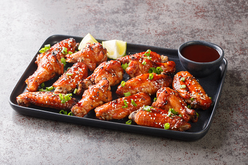 Chinese stir-fried chicken wings in sweet spicy Hoisin sauce with sesame close-up on a plate on the table. Horizontal