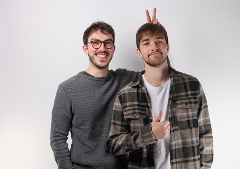 portrait of two young adults in their 20s. One of them pranks his friend by making bunny ears with his hand.