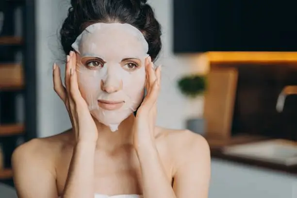 Photo of Caucasian girl applies mask sheet after bathing. Vitamin, nourishing and nutrition face mask.