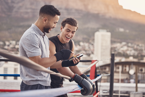 Boxer and coach with phone after training, exercise or workout reading social media meme online. Sport athlete smile and laugh after coaching mma, muay thai and boxing outdoor in a fighting ring