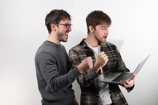 two friends or colleagues are standing with a laptop. They clench their fist as a sign of success or victory