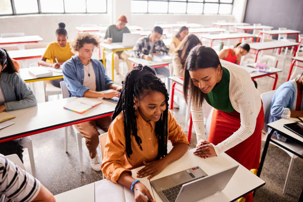istock Smiling teacher working with a student using a laptop in a classroom 1440718611