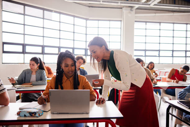 istock Smiling teacher working with a student using a laptop during a classroom lesson 1440718788
