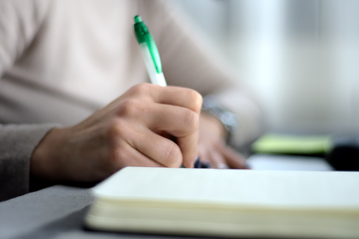 a woman's hand writing in a notebook or diary using a green and white ballpoint pen. selective focus