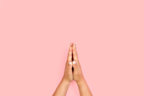 istock Woman hands in praying gesture on a pink background 1440719507