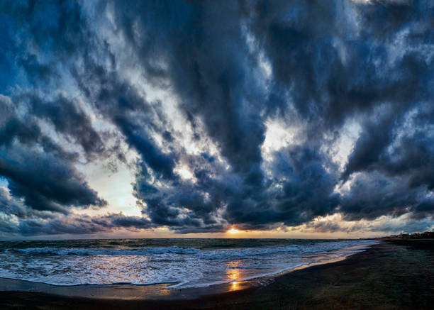Fantastic stormy sky and dramatic weather panoramic view over the beach , impressive blue hour with golden sunbeams hits rough foamy threatening sea  waves crashing at the shore.