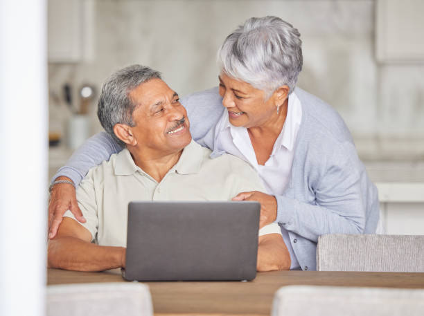 istock Happy elderly couple streaming on laptop, hug and bonding while relax in kitchen at home. Senior man and woman indoors, enjoy retirement and relationship, talking while browsing for subscription 1440723081
