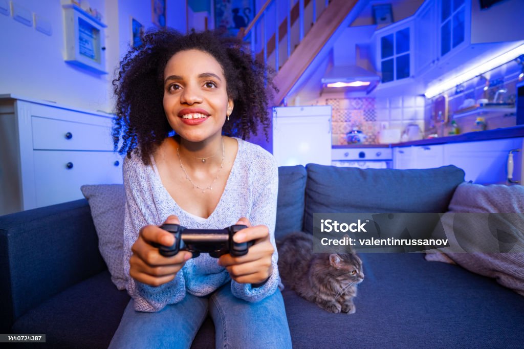 Smiling african-american  young woman enjoying videogame on playstation, having fun at home on the evening One Woman Only Stock Photo