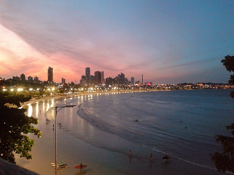The view of Ponta Negra Beach, located in the state of Rio Grande do Norte, Brazil, at dusk. View from the top. City lights reflected on the beach water.