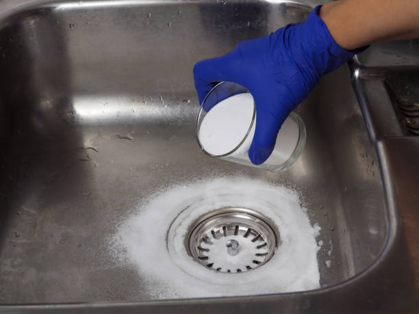 istock Gloved hand putting baking soda on drain In sink from glass jar 1440725603