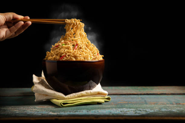 Bow of Hot Boiled Instant Noodles on the Table. Hand Using Chopsticks to Eating Noodles with Stream. Cheap Fast food Concepts. Side View with more Copy Space stock photo