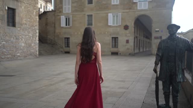 Caucasian model in a red dress walking through the city of Vitoria, Araba. Spain