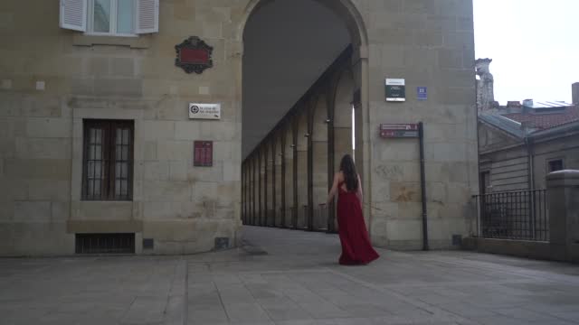 Caucasian model in a red dress walking through the city of Vitoria, Araba. Spain