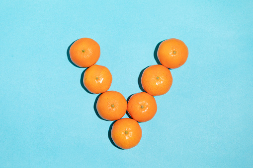 Juicy, healthy and irregular shaped tangerines, forming the letter V on a blue background, giving rise to a pop art style image and texture