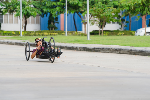 Physically impaired male athlete in helmet training in racing wheelchair for adaptive exercise outdoors.
