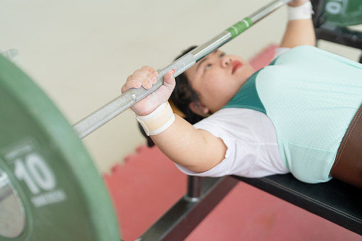 Young disabled woman athlete performing a bench press with a barbell.