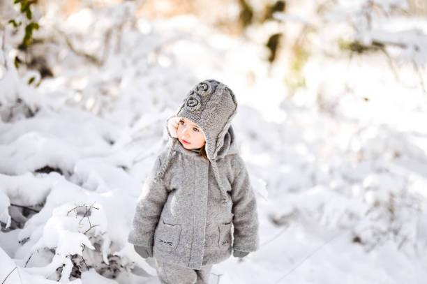 Small adorable beautiful caucasian baby girl in a snowy Park. Girl winter portrait. Children 18-23 months.