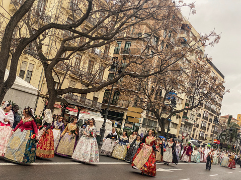 Valencia, Spain - March 17, 2022: Long row of young women in the street wearing traditional dresses to celebrate Las Fallas. This is an annual event happening in the Valencian Community during the month of March