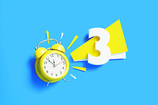 Number three sitting next to yellow alarm clock on blue background. Horizontal composition with copy space.