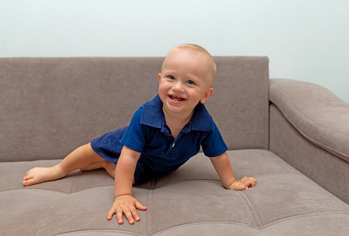 A smiling little boy playfully looks at the camera while sitting on the couch at home. Safe happy childhood