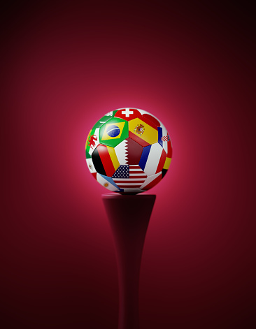 Soccer ball textured with national flags sitting on cherry colored podium before cherry colored background. Vertical composition with copy space.